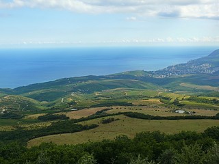 Photo of mountains in the Crimea, covered with green forests and grass, and shrouded in white clouds. In the distance you can see the town and the view of the Bl