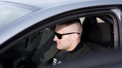 Fototapeta na wymiar Side view of confident young stylish man in sunglasses driving his car