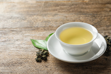 Cup of Tie Guan Yin oolong and tea leaves on wooden table. Space for text