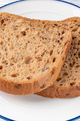 Slices of grain bread with mold. On a white plate with a blue stripe. On a wooden table