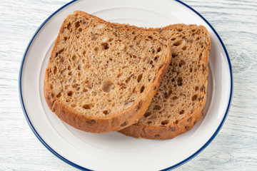 Slices of grain bread with mold. On a white plate with a blue stripe. On a wooden table
