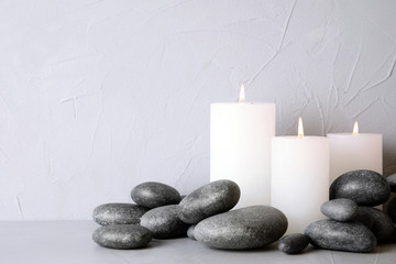 Fototapeta na wymiar Zen stones and lighted candles on table against light background. Space for text