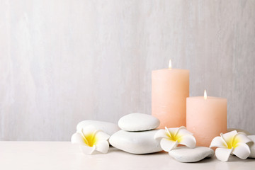 Fototapeta na wymiar Zen stones, lighted candles and exotic flowers on table against light background. Space for text