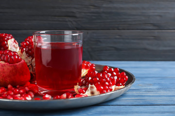 Tray with glass of pomegranate juice and fresh fruits on table against wooden background, space for text