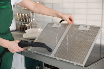 Professional janitor cleaning mesh filter of cooker hood in kitchen, closeup