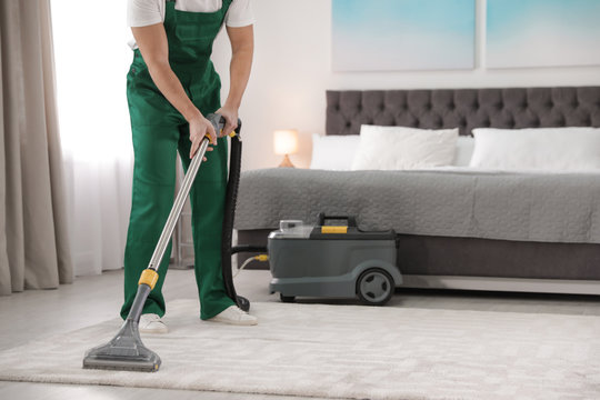 Professional janitor removing dirt from carpet with vacuum cleaner in bedroom, closeup. Space for text