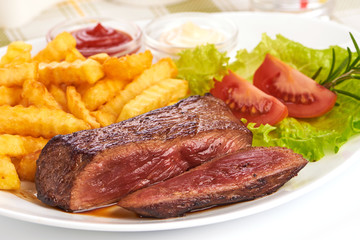 Grilled medium rare beef steak with french fries, sliced fried meat, close-up