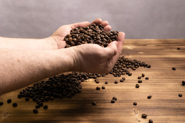 Coffee beans in hands on wooden background