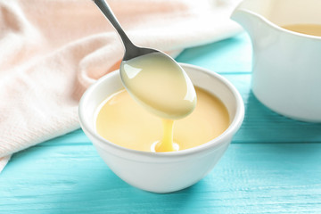 Spoon of pouring condensed milk over bowl on table. Dairy products
