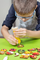 Skupiona twarz chłopca w okularach, który dekoruje ciastko w kształcie serca za pomocą lukru w tubce
