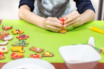 Obraz na płótnie Canvas Chłopiec dekoruje cynamonowe ciastko. Trzyma w dłoniach tubkę z lukrem w kolorze czerwonym i wyciska na ciastko.