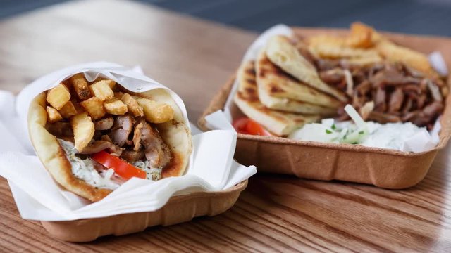 Big traditional Greek cuisine dinner served on table in paper plate.Fast food medditeranean restaurant menu dishes.Enjoy roasted meat souvlaki dish & fried gyros roll.Junk food menu
