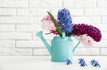 Beautiful hyacinths in watering can on table against brick wall, space for text. Spring flowers