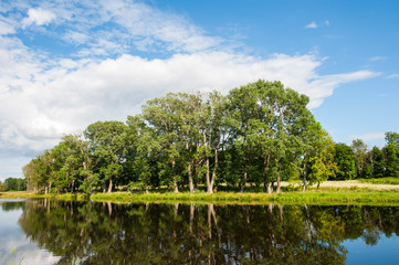 Beautiful still lake with trees on the horizon and white puffy clouds in the sky. Peaceful summer...