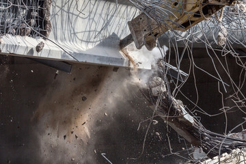 Professional demolition of reinforced concrete structures using industrial hydraulic hammer. Rods of metal fittings. Wreckage and crumbles of concrete.