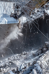 Professional demolition of reinforced concrete structures using industrial hydraulic hammer. Rods of metal fittings. Wreckage and crumbles of concrete.