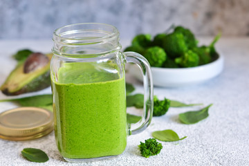 Green smoothie with spinach, avocado and broccoli on a concrete background.