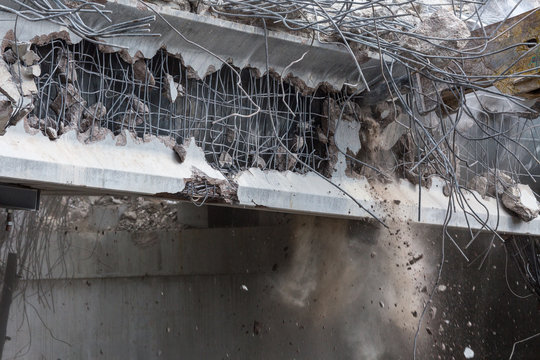 Professional demolition of reinforced concrete structures using industrial hydraulic hammer. Rods of metal fittings. Wreckage and crumbles of concrete.