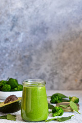 Green smoothie with spinach, avocado and broccoli on a concrete background.