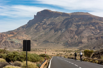 Cyclist cycling on a road through volcanic landscape.