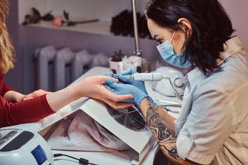 Hardware manicure in a beauty salon. Manicure procedure in progress - Beautician master using nail drill to trim and remove cuticles