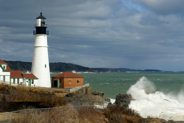 Fototapeta na wymiar Sunlight Breaks Through Clouds on Portland Head Lighthouse with Huge Waves Breaking in Maine