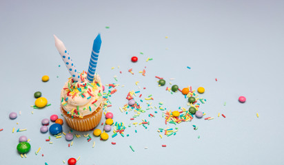 Cupcake vanilla with two candles on blue pastel background, copy space.