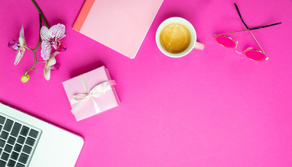 Flowers,  cup of coffee and laptop on pink desk background, copy space