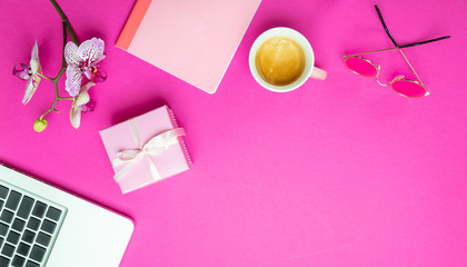 Flowers,  cup of coffee and laptop on pink desk background, copy space