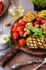 Grilled vegetables on cutting board on wooden background. Grilled vegetables (colorful bell pepper, tomatoes, onion, zucchini, eggplant) with basil