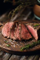 Juicy medium Beef Rib Eye steak slices on wooden board with herbs spices and salt.