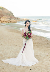 Fototapeta na wymiar pretty bride in luxury wedding dress with bouquet at the sea side. Wedding by the sea. Bride walking around the sea near the place of the wedding ceremony.
