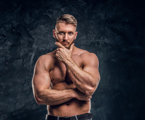 Fototapeta na wymiar Bearded shirtless male with muscular body posing with hand on chin. Studio photo against dark wall background