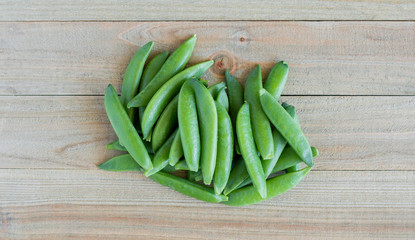 a small bunch of green sugar snap peas on a wood background viewed from above
