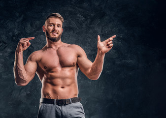 Cheerful shirtless man with the muscular body posing for a camera. Studio photo against dark wall background