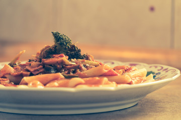 Penne with tomato sauce pork panceta broccoli and mashrooms served to the plate and ready to be placed to the family lunch table
