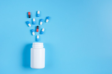 Blue and white pills, tablets and white bottle on blue background.  Alien among theirs.