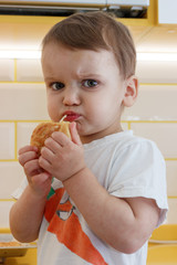 Two years old baby eats cookies in the kitchen