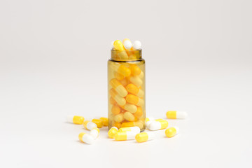 Medicine white and yellow pills or tablets drop out of the brown glass bottle on white background.
