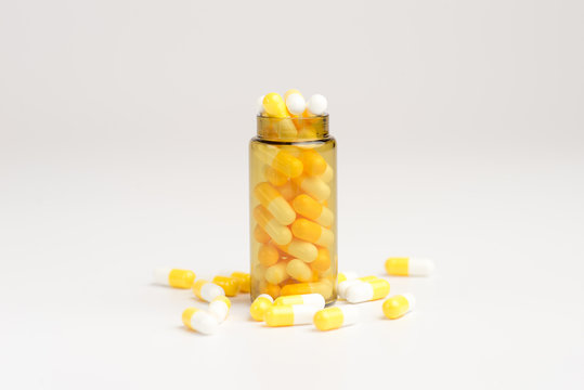 Medicine white and yellow pills or tablets drop out of the brown glass bottle on white background.