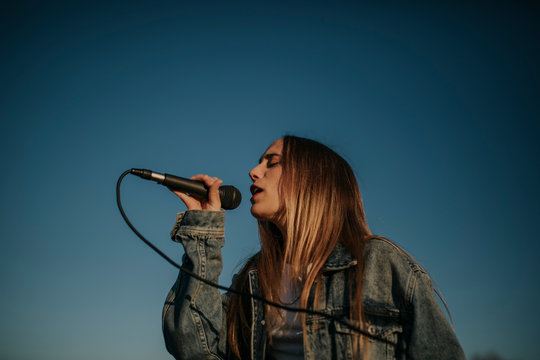 Young woman singing with a microphone under blue sky