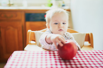 Cute baby girl eating apple in the kitchen