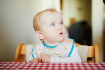 Cute baby girl eating carrot in the kitchen