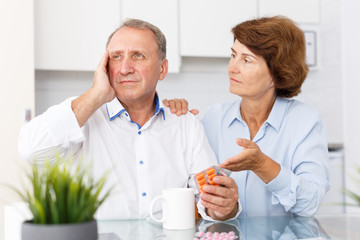 Sad mature family couple with  medicine sitting at kitchen table