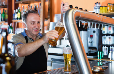 Barman is pouring unbottled beer with foam for client in the bar