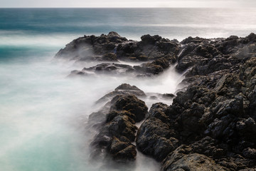 Long exposure of deep blue water, swirling surf, and rocky cliffs of central California