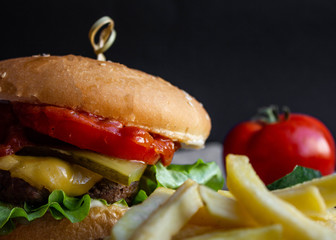 fresh tasty cheese burger with french fries and vegetables on black background