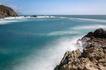 Long exposure of deep blue water, swirling surf, and rocky cliffs of central California