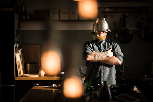 Man standing in kitchen, wearing colander as helmet