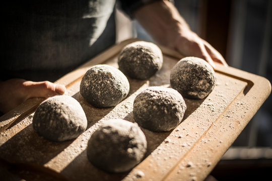 Man preparing black burger buns in kitchen, letting dough rise